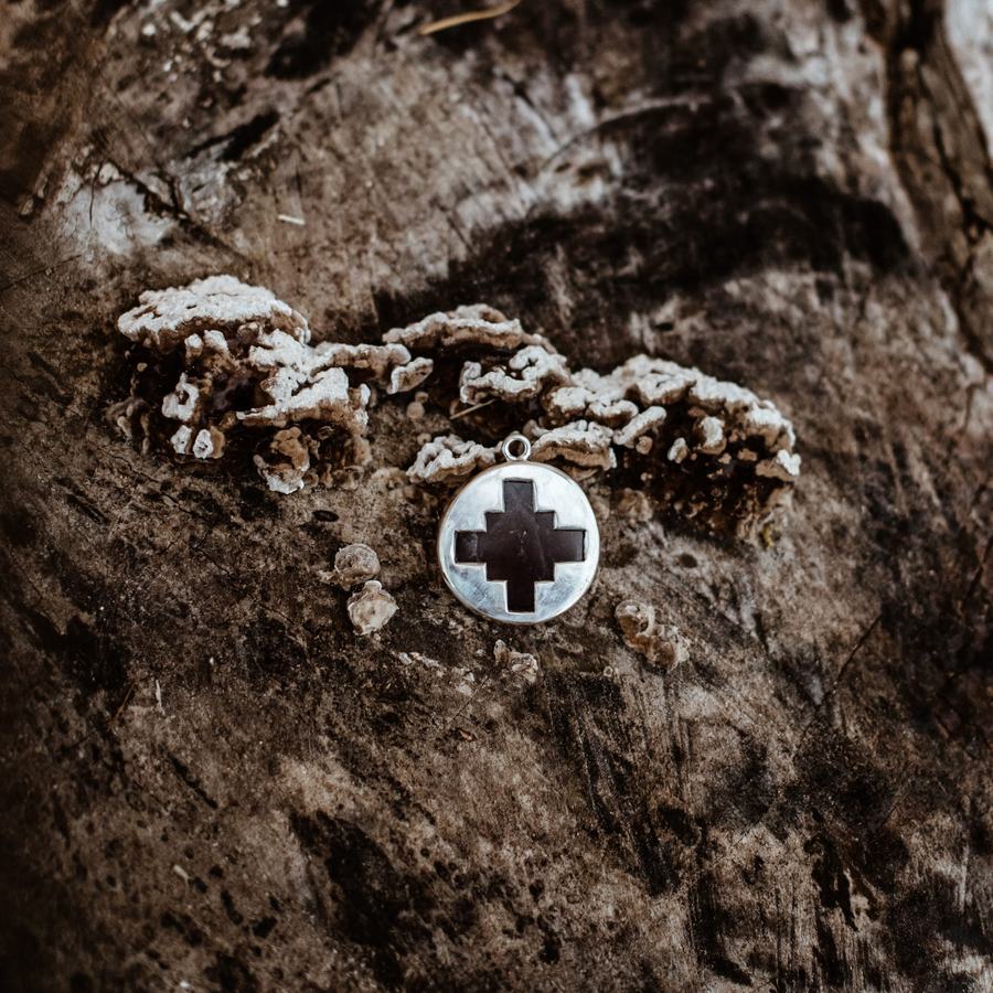 Silver amulet with inlaid dark cross on tree fungus