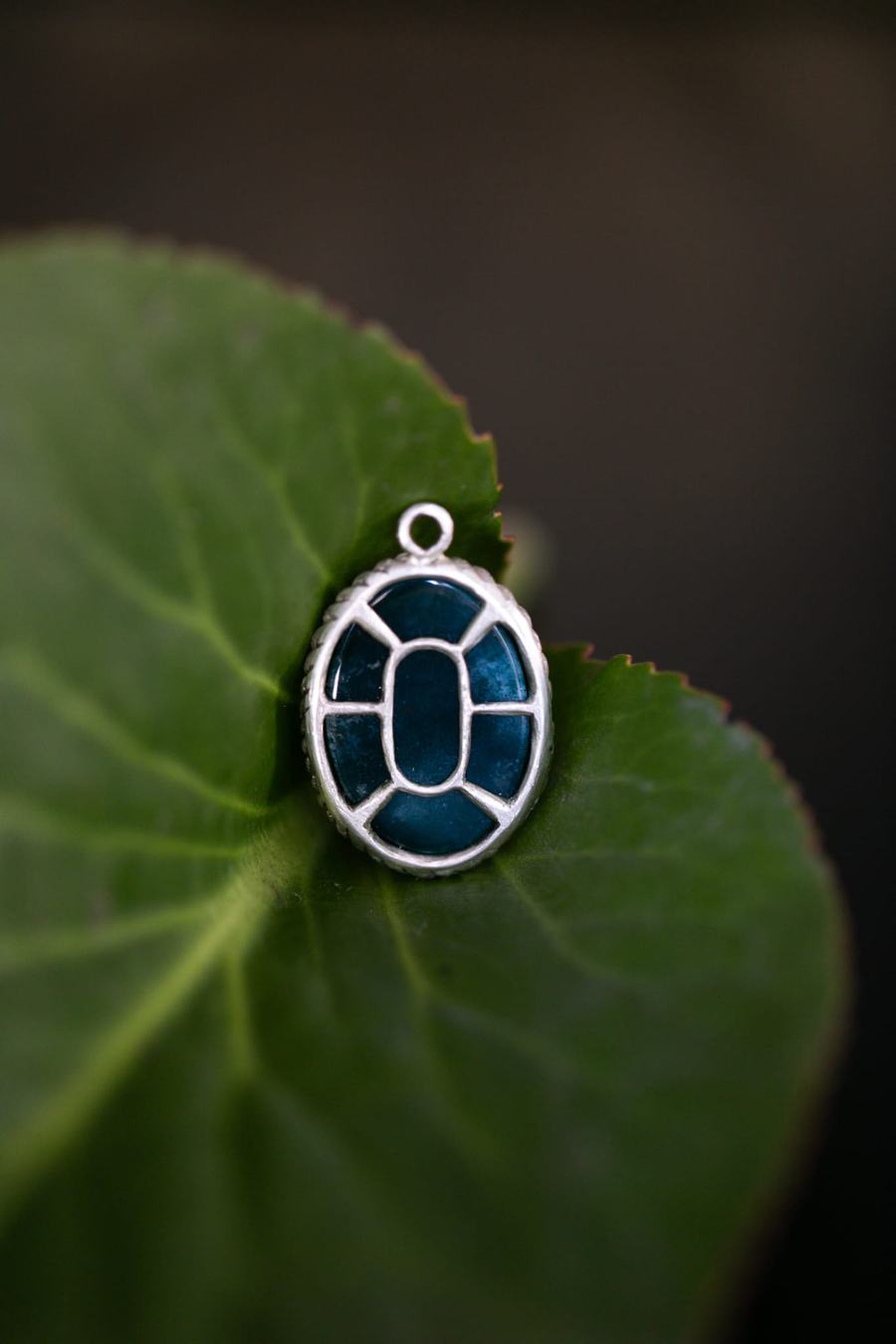 Deep teal stone pendant in silver bezel on a leaf